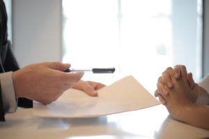 Person handing a pen and document to another person