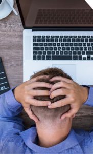Migraines Injury Compensation, stressed man with his hands on his head using a laptop