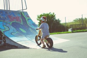 little boy in a helmet riding a small wooden bike in a skate park
