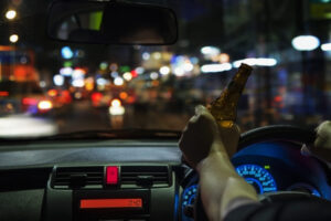 Cropped Of Man Drinking Beer While Driving Car In City At Night